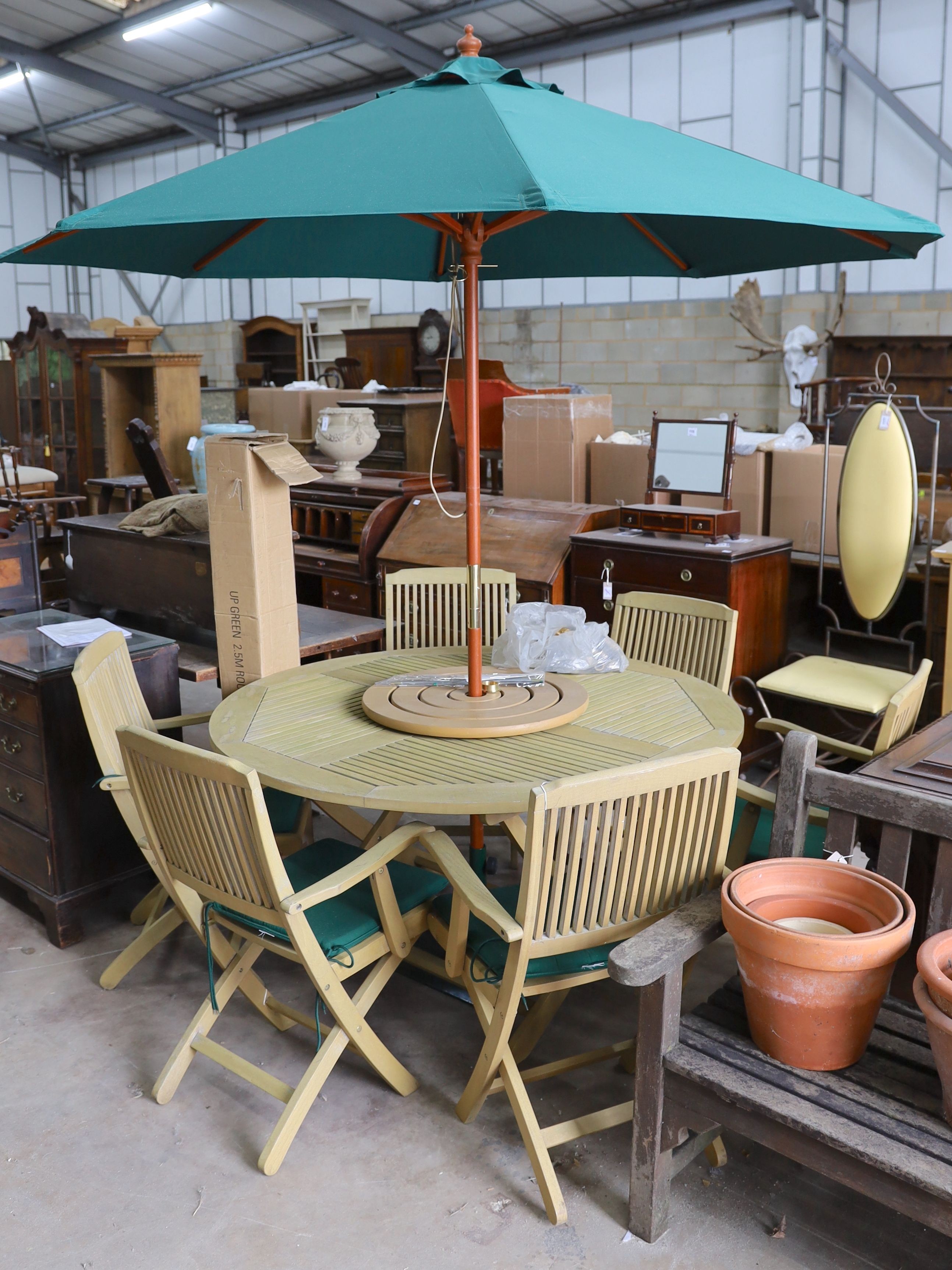 A teak garden set comprising circular table 148 cms diameter height 75 cms with 'Lazy Susan', parasol and waterproof cover and metal base, six folding elbow chairs and seat cushions.
